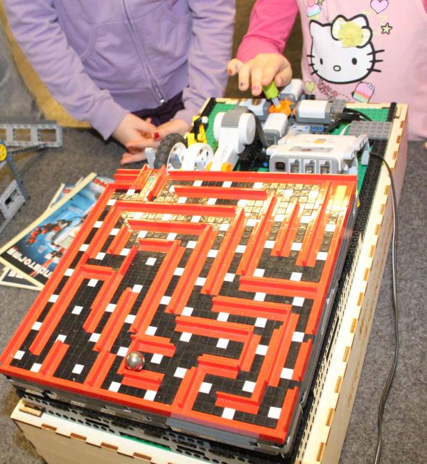 Zwei Kinder spielen mit einem motorisierten Labyrinth aus Legosteinen.