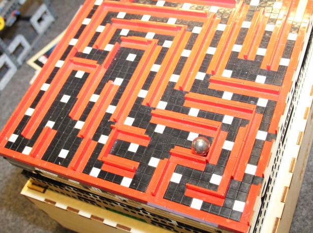 Eine Metallkugel liegt in einem Labyrinth aus roten Stegen auf einem Spielbrett.