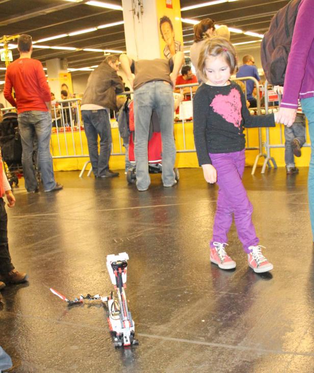 Ein Mädchen steht neben einem umgefallenen Lego-Roboter auf dem Boden.