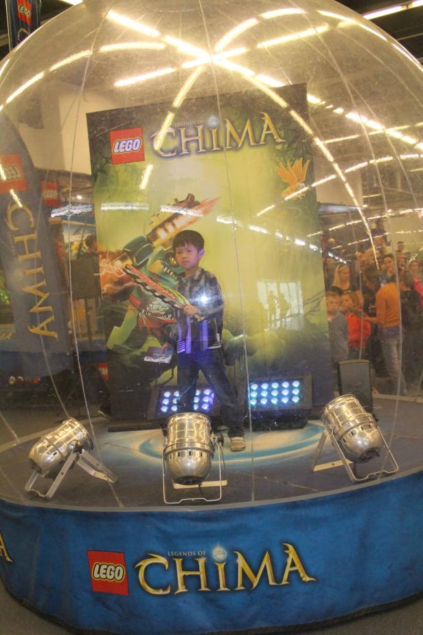Ein Junge posiert vor einem „Lego Legends of Chima“-Hintergrund in einer transparenten Kuppel.