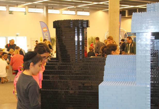 Besucher betrachten ein großes Bauwerk aus schwarzen und hellblauen Legosteinen.