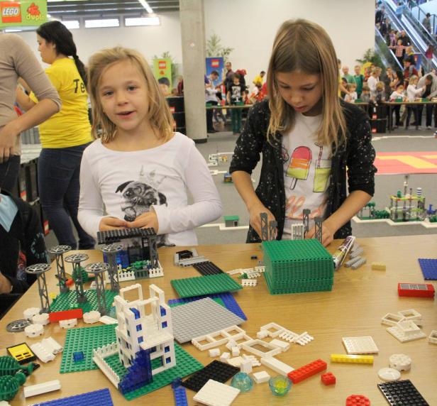 Zwei Mädchen bauen mit Legosteinen auf einem Tisch.