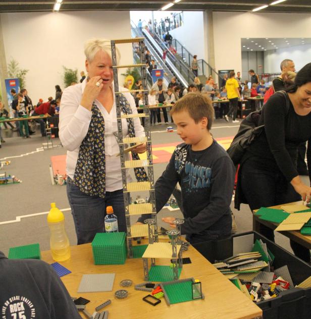 Eine Frau und ein Kind bauen gemeinsam einen hohen Turm aus Legosteinen.