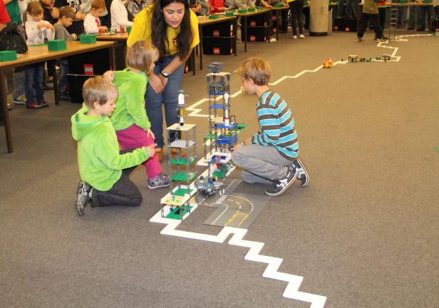 Kinder bauen mit einer Betreuerin ein mehrstöckiges Gebäude aus Lego.