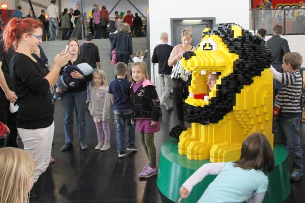 Besucher interagieren mit einer großen Löwenskulptur aus Legosteinen.