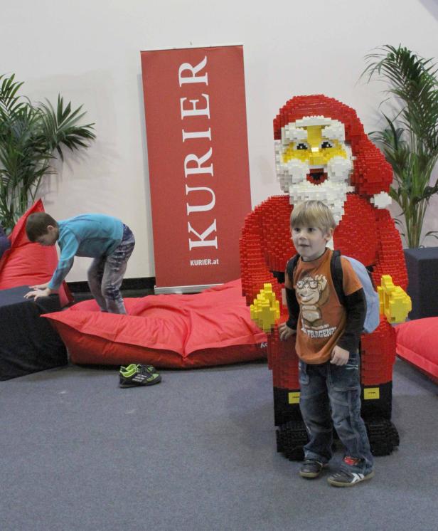 Ein Junge steht neben einer großen, aus Legosteinen gebauten Weihnachtsmannfigur.
