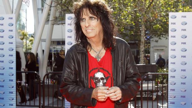 Alice Cooper trägt eine Lederjacke und ein rotes T-Shirt mit Totenkopf-Motiv.