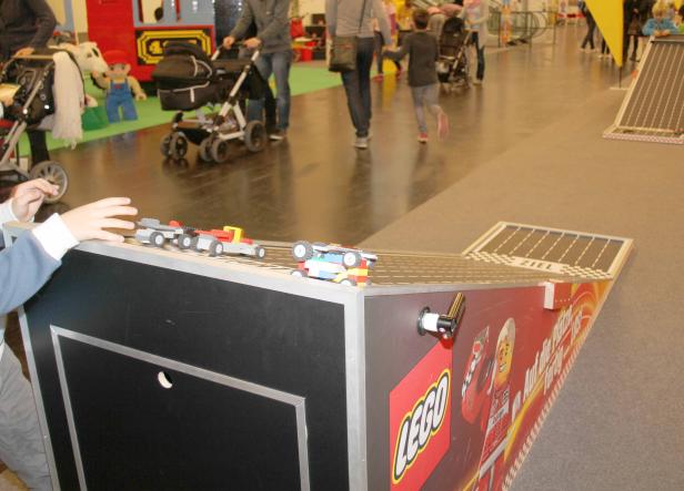 Kinder spielen mit Lego-Autos auf einer Rampe mit Ziellinie.