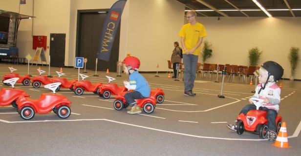 Kinder fahren mit roten Spielzeugautos auf einem Parcours mit Verkehrszeichen.