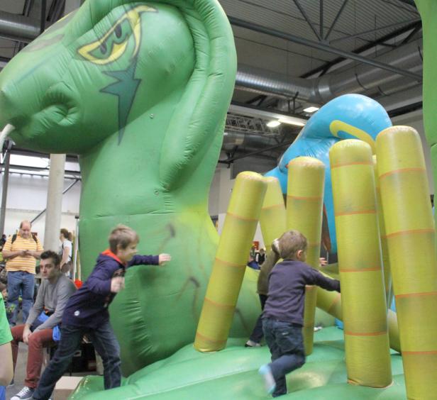 Kinder spielen auf einer aufblasbaren Hüpfburg in Form eines grünen Drachen.