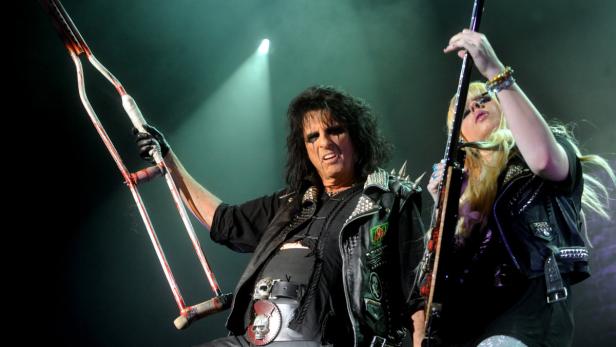 Alice Cooper mit blutverschmierten Krücken auf der Bühne, neben einer Gitarristin.