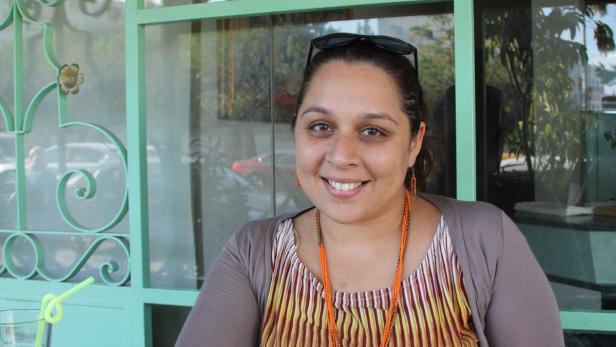 Eine lächelnde Frau sitzt vor einem Fenster mit mintgrünem Rahmen.