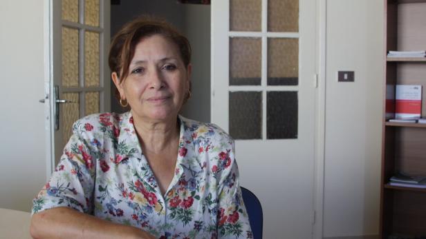 Eine Frau mit braunen Haaren und einer geblümten Bluse sitzt an einem Tisch.