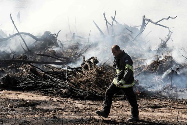 Ein Feuerwehrmann geht durch ein zerstörtes, rauchendes Gebiet.