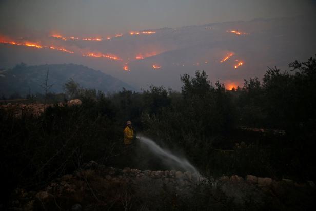 Eine Person in Schutzkleidung bekämpft einen Waldbrand mit einem Wasserstrahl.