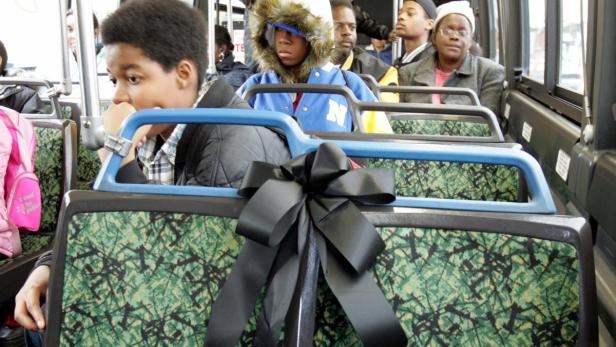 Fahrgäste sitzen in einem Bus, dessen Sitze mit einer schwarzen Schleife geschmückt sind.