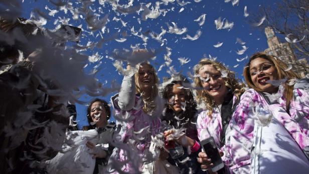 Eine Gruppe junger Frauen nimmt an einer Kissenschlacht im Freien teil, Federn fliegen in der Luft.