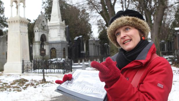 Eine Frau in Winterkleidung führt eine Tour über einen verschneiten Friedhof.