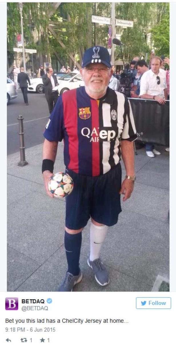 Ein älterer Mann in einem Trikot, das aus zwei verschiedenen Fußballtrikots zusammengenäht ist, hält einen Fußball.