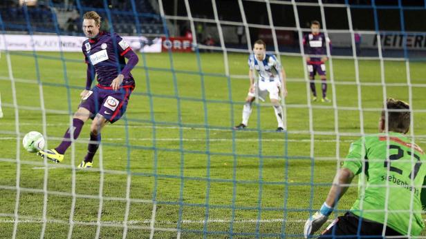 Ein Fußballspieler schießt den Ball ins Tor, während der Torwart zusieht.