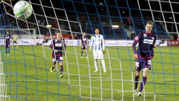 Ein Fußball fliegt ins Netz, während ein Spieler jubelt.