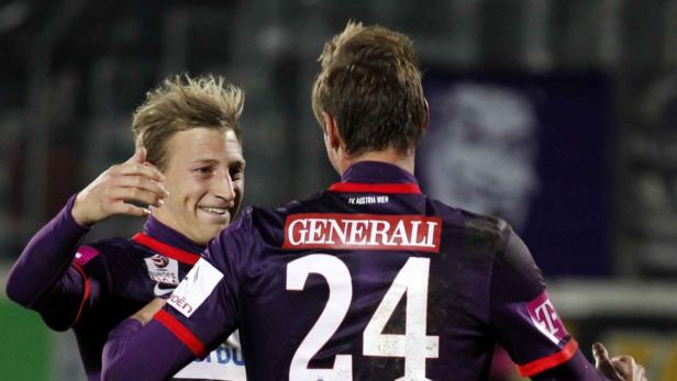 Zwei Fußballspieler von FK Austria Wien umarmen sich auf dem Spielfeld.