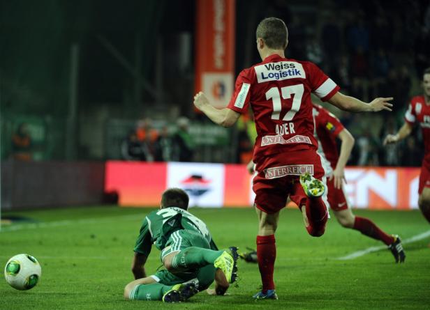 Ein Fußballspieler in Rot läuft, während ein anderer in Grün am Boden liegt.