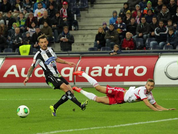 Ein Fußballspieler grätscht, um den Ball vor einem anderen Spieler zu erreichen.