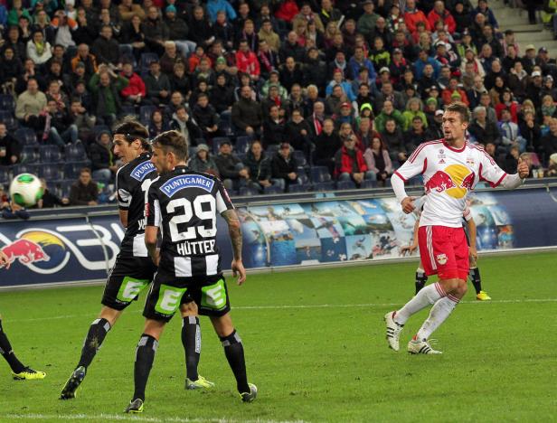 Ein Fußballspieler jubelt auf dem Spielfeld, während andere Spieler und Zuschauer im Hintergrund zu sehen sind.