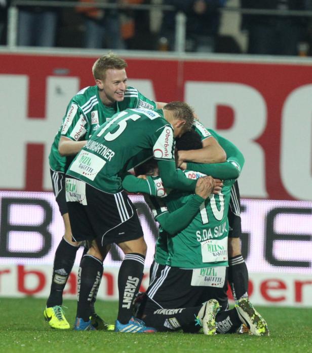 Fußballspieler in grünen Trikots umarmen sich auf dem Spielfeld.