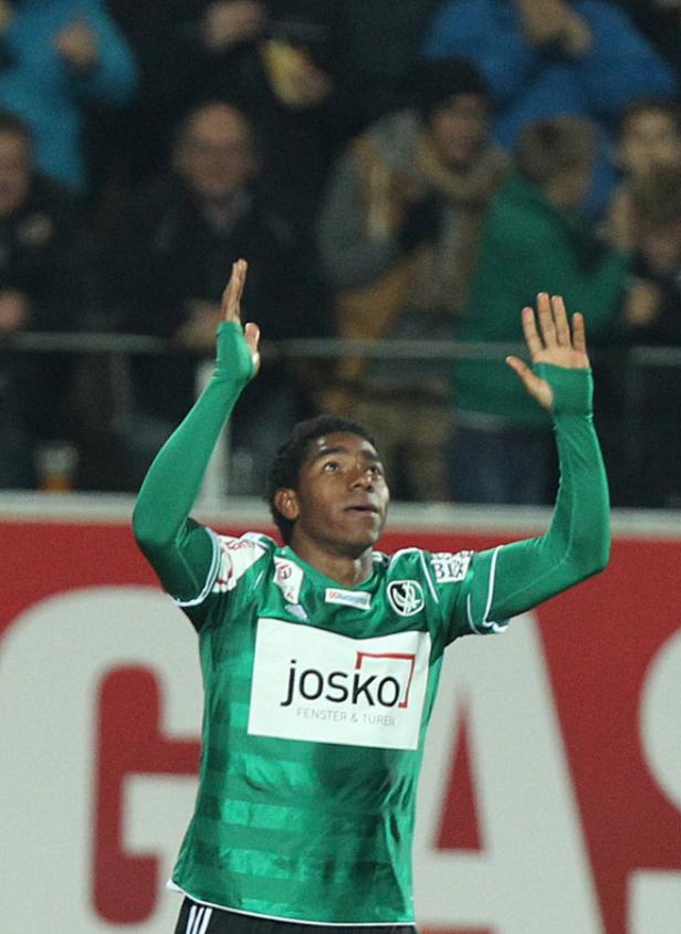 Ein Fußballspieler in einem grünen Trikot jubelt mit erhobenen Armen.