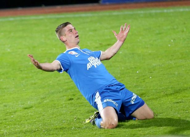 Ein Fußballspieler jubelt auf dem Rasen, die Arme nach oben gestreckt.