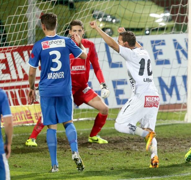 Ein Fußballspieler jubelt vor dem Tor, während der Torwart und ein Verteidiger zusehen.