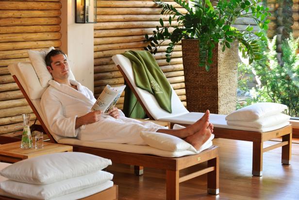 Ein Mann im Bademantel liest entspannt auf einer Liege in einem Wellnessbereich.