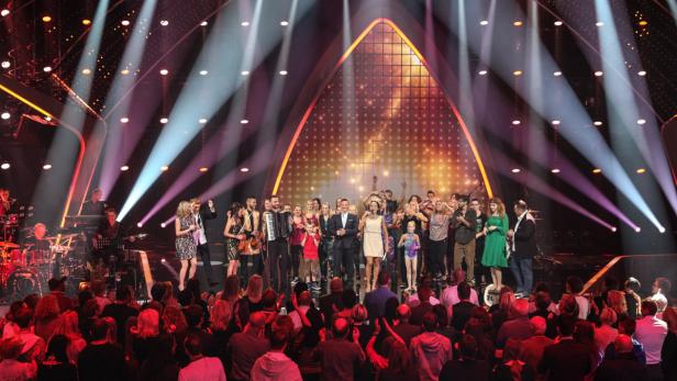 Eine Gruppe von Musikern und Sängern steht auf einer Bühne vor einem Publikum.