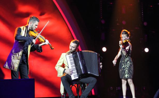 Drei Musiker spielen Geige und Akkordeon auf einer Bühne.