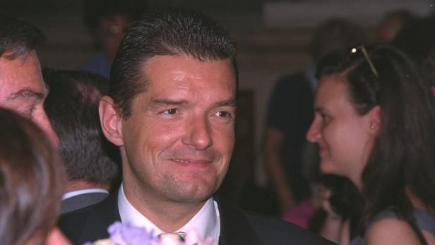 Ein lächelnder Mann im Anzug, umgeben von anderen Personen.