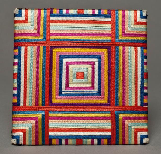 Ein quadratisches Objekt, umwickelt mit bunten Fäden in einem geometrischen Muster.