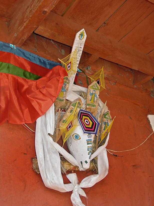 Eine dekorative Maske mit religiösen Motiven hängt an einer roten Wand.