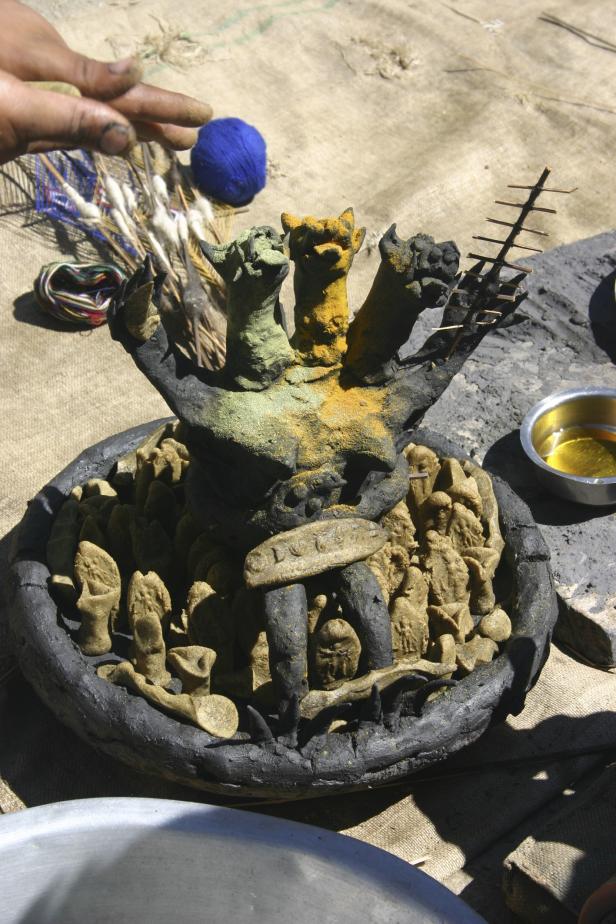 Eine dreiköpfige, farbige Skulptur in einer Schale mit kleinen Figuren.