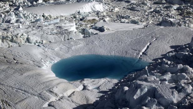 Ein tiefblauer Schmelzwassertümpel auf einer eisigen, schneebedeckten Landschaft.