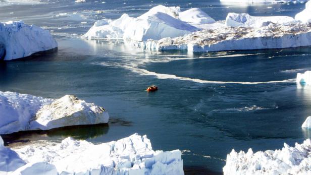 Ein kleines Boot fährt zwischen großen Eisbergen hindurch.