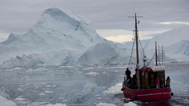 Ein rotes Boot fährt durch eisiges Wasser vor einer Gletscherlandschaft.