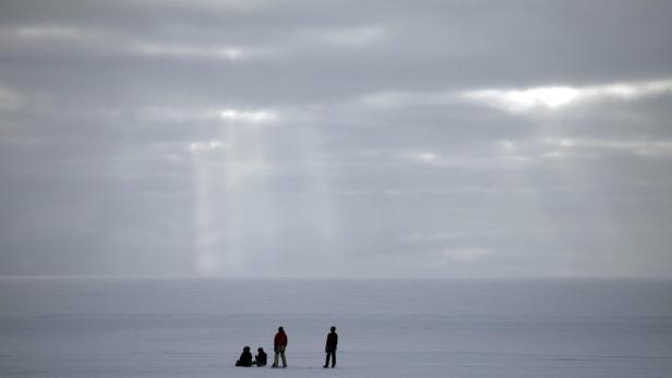 Eine Gruppe von Menschen steht auf einer weiten, schneebedeckten Fläche unter einem bewölkten Himmel.