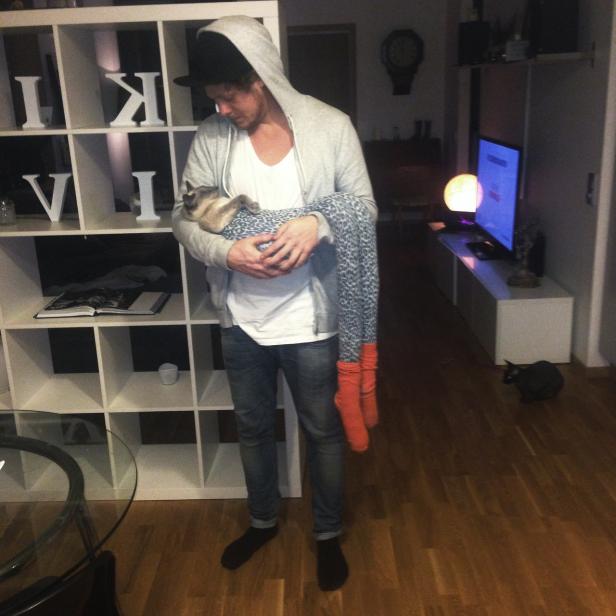 Ein Mann hält eine Katze in einer gemusterten Decke im Arm.