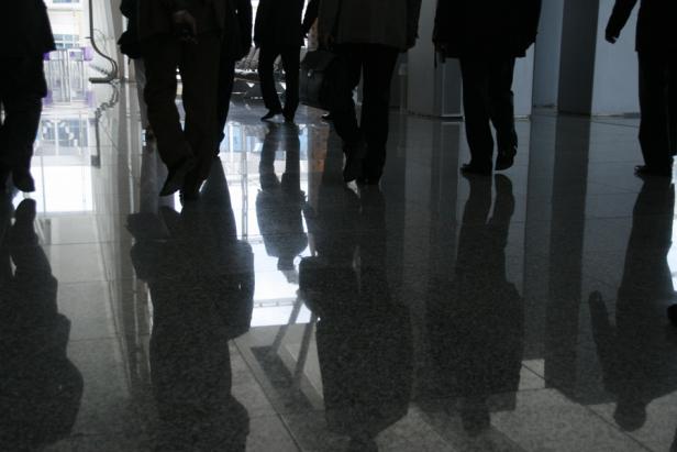 Menschen gehen auf einem glänzenden Boden, ihre Schatten spiegeln sich wider.