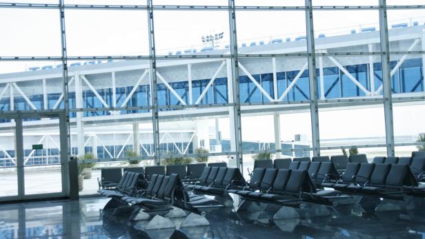 Leere Sitzreihen in einem Wartebereich mit großen Fenstern in einem Flughafen.