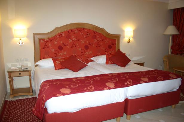 Ein Hotelzimmer mit zwei Betten, roter Bettwäsche und gemustertem Kopfteil.