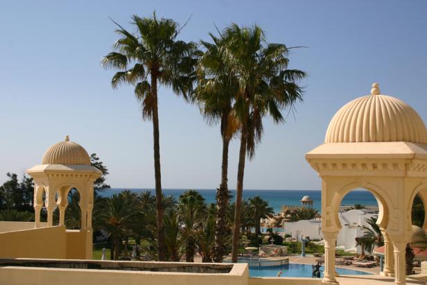 Palmen und Pavillons prägen die Ansicht eines Resorts am Meer.