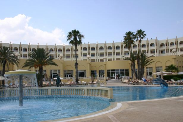 Ein Hotelresort mit Pool, Springbrunnen und Palmen unter blauem Himmel.